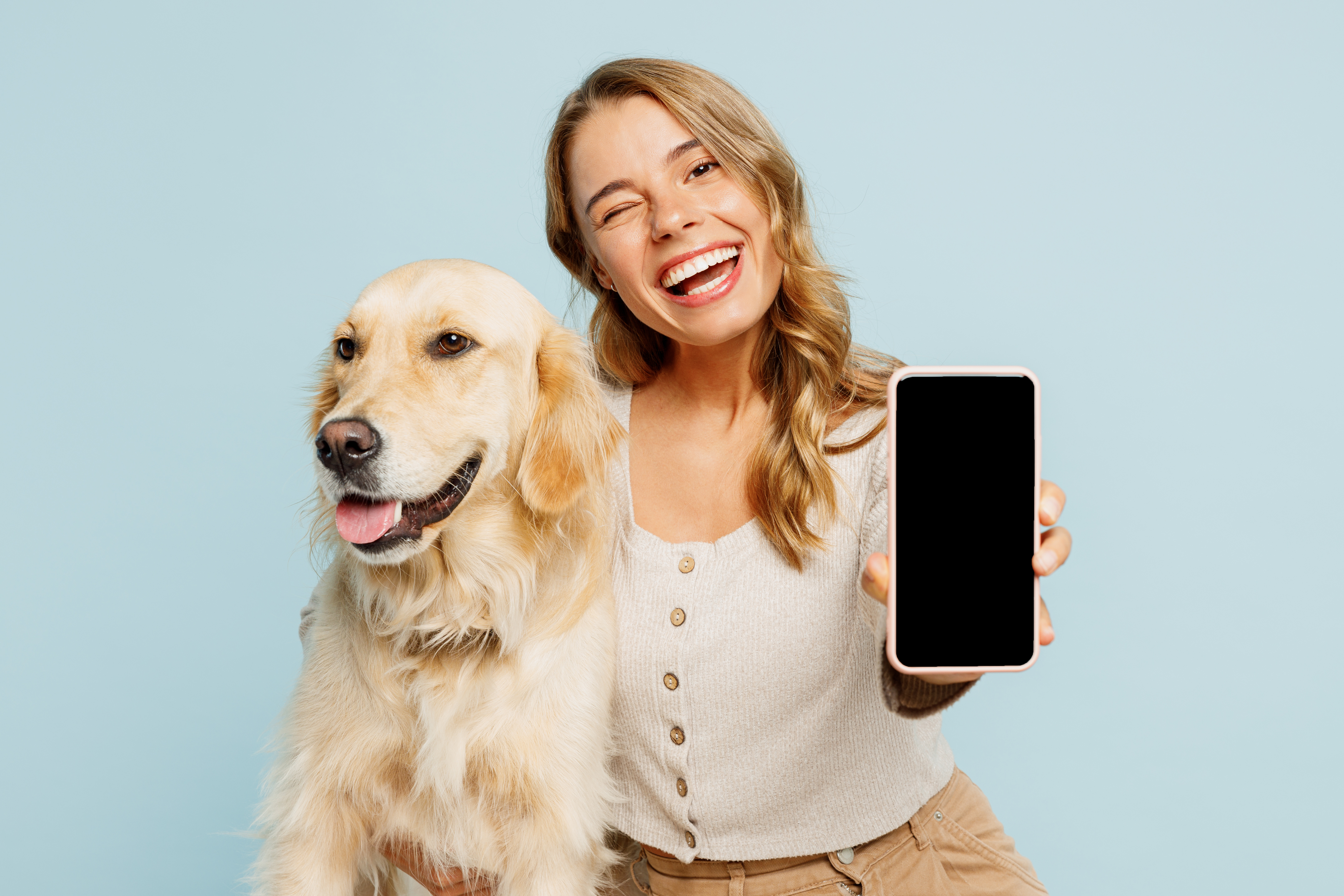 Woman holding a golden retriever while showing a phone